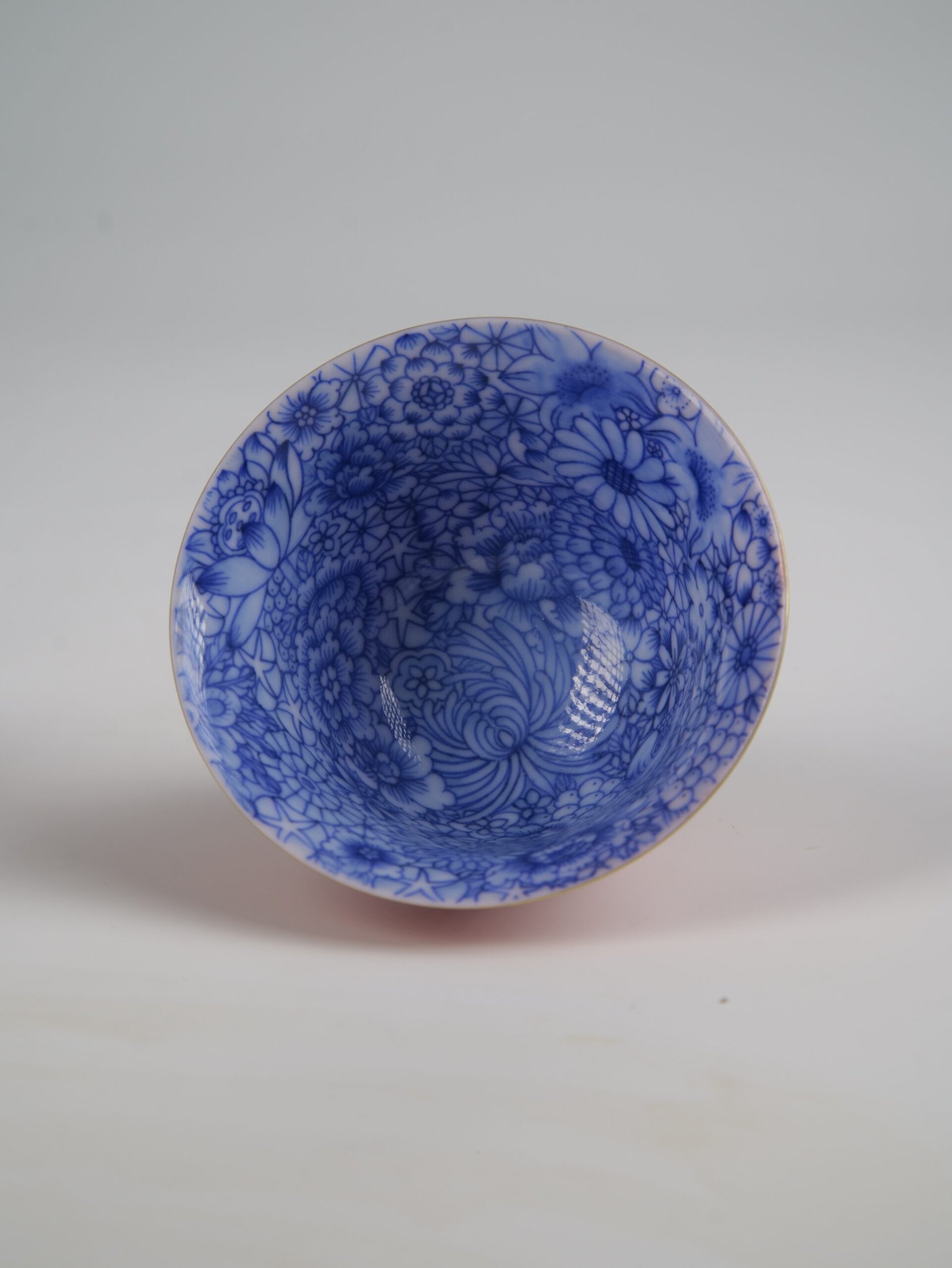 palace-red-elegant-charm-gaiwan-blue-floral-interior A close-up top-down view of the inside of the Palace Red Elegant Charm Gaiwan cup, highlighting the hand-painted blue and white floral pattern covering the interior.