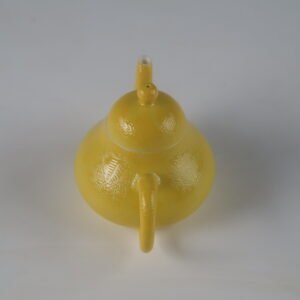 High angle rear perspective view showing the handle and lid knob of a bright yellow pear teapot