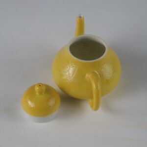 Top-down view of open bright yellow pear teapot showing interior filter holes and lid on white background
