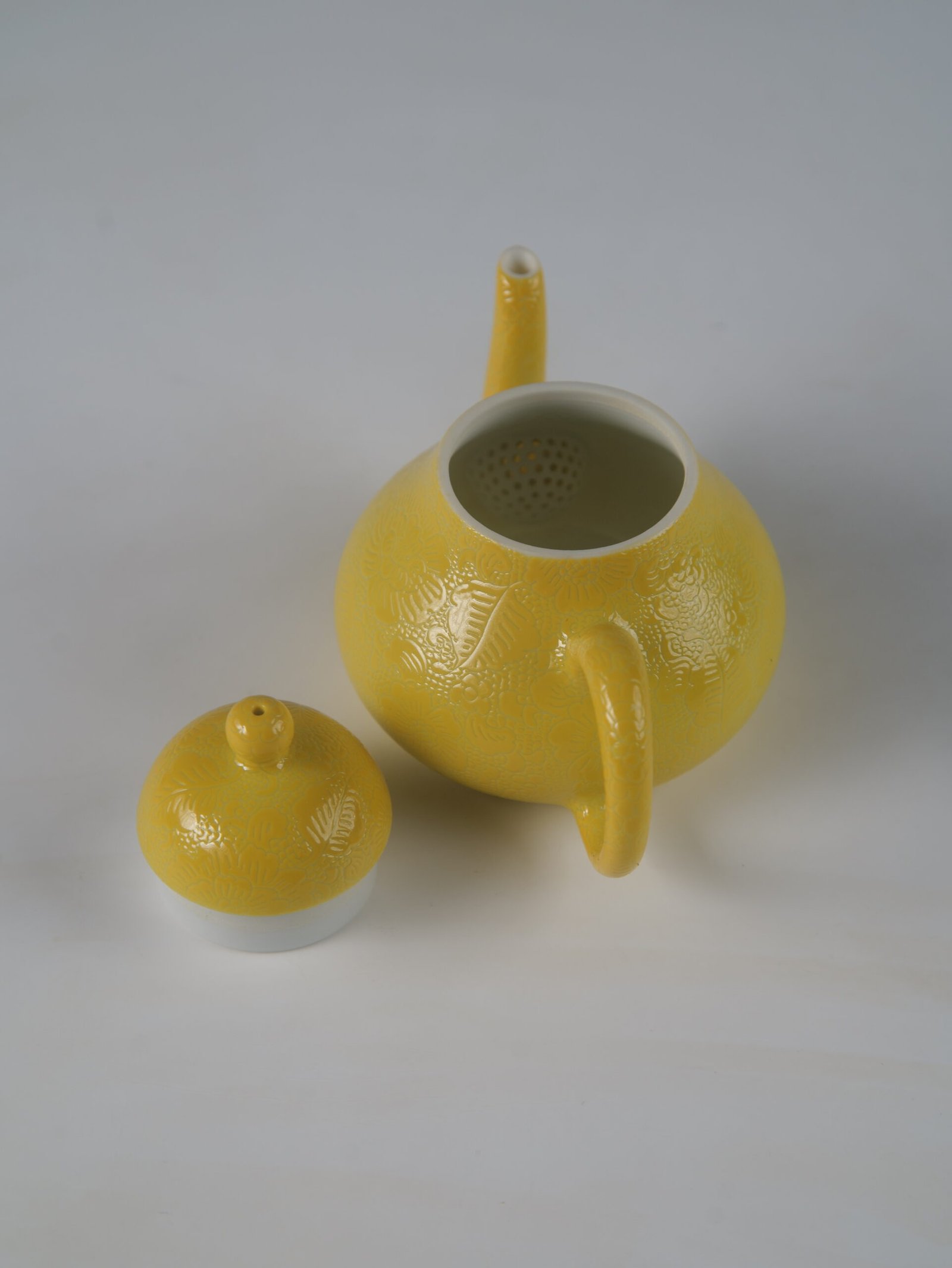 Bright Yellow Pear Teapot – Interior and Filter Detail Top-down view of open bright yellow pear teapot showing interior filter holes and lid on white background