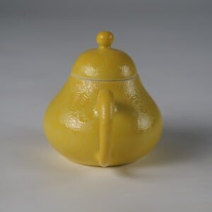 Eye-level rear view facing the handle of a bright yellow pear-shaped porcelain teapot
