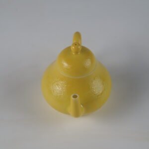 High angle front perspective view facing the spout of a bright yellow pear-shaped porcelain teapot