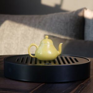 Bright yellow pear teapot with hand-carved hundred flowers pattern placed on a black tea tray in living room setting