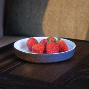 Carved porcelain plate holding fresh red strawberries on wooden table
