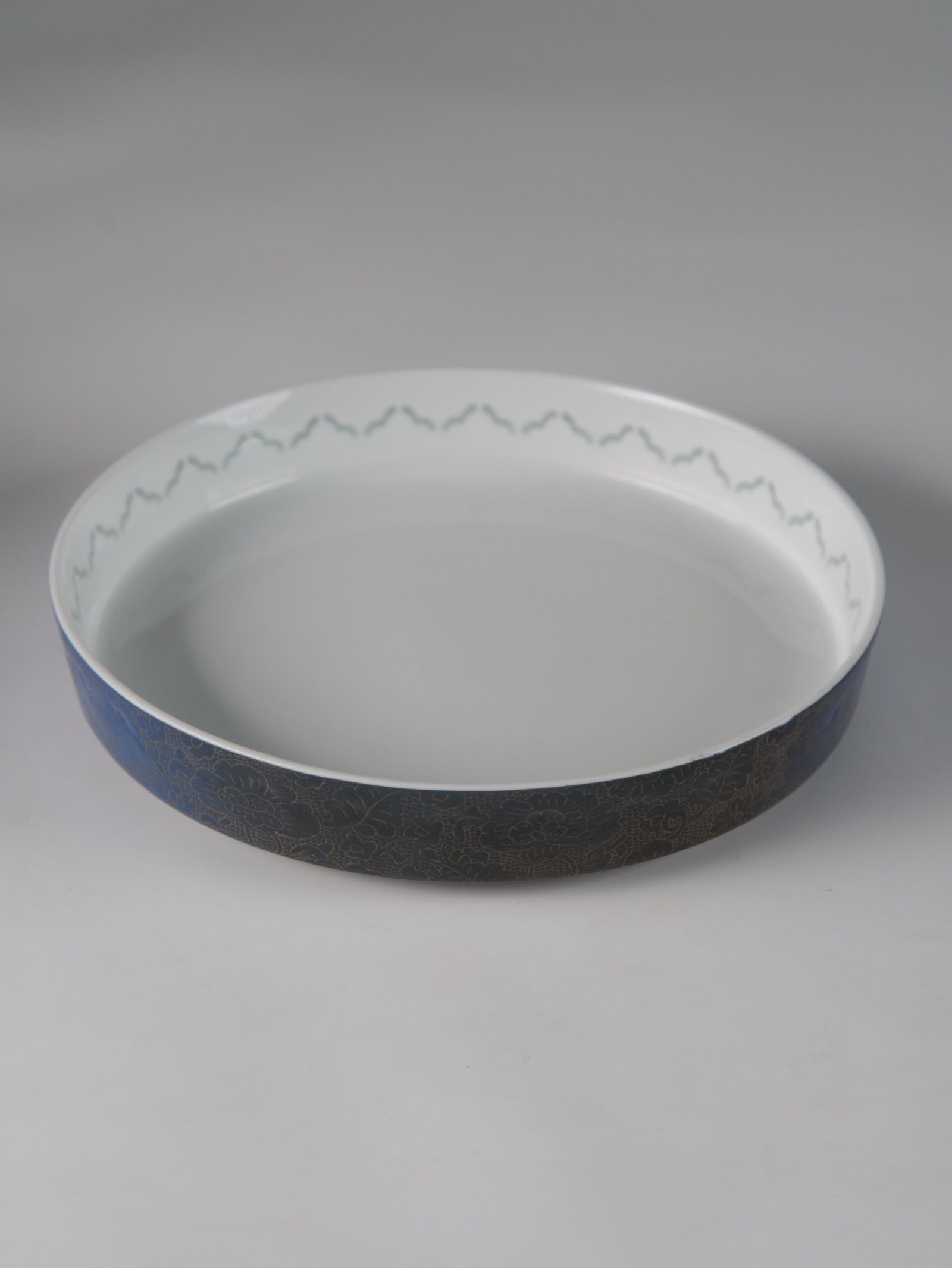 Carved Linglong Porcelain Plate – Angle View Angled top view of porcelain plate showing carved exterior pattern and white interior