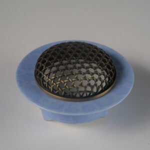 Angled view of light blue ceramic incense burner with woven copper lid