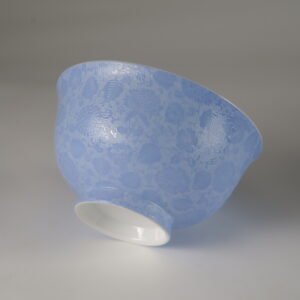 Tilted view of light blue porcelain bowl displaying carved flower texture and foot rim