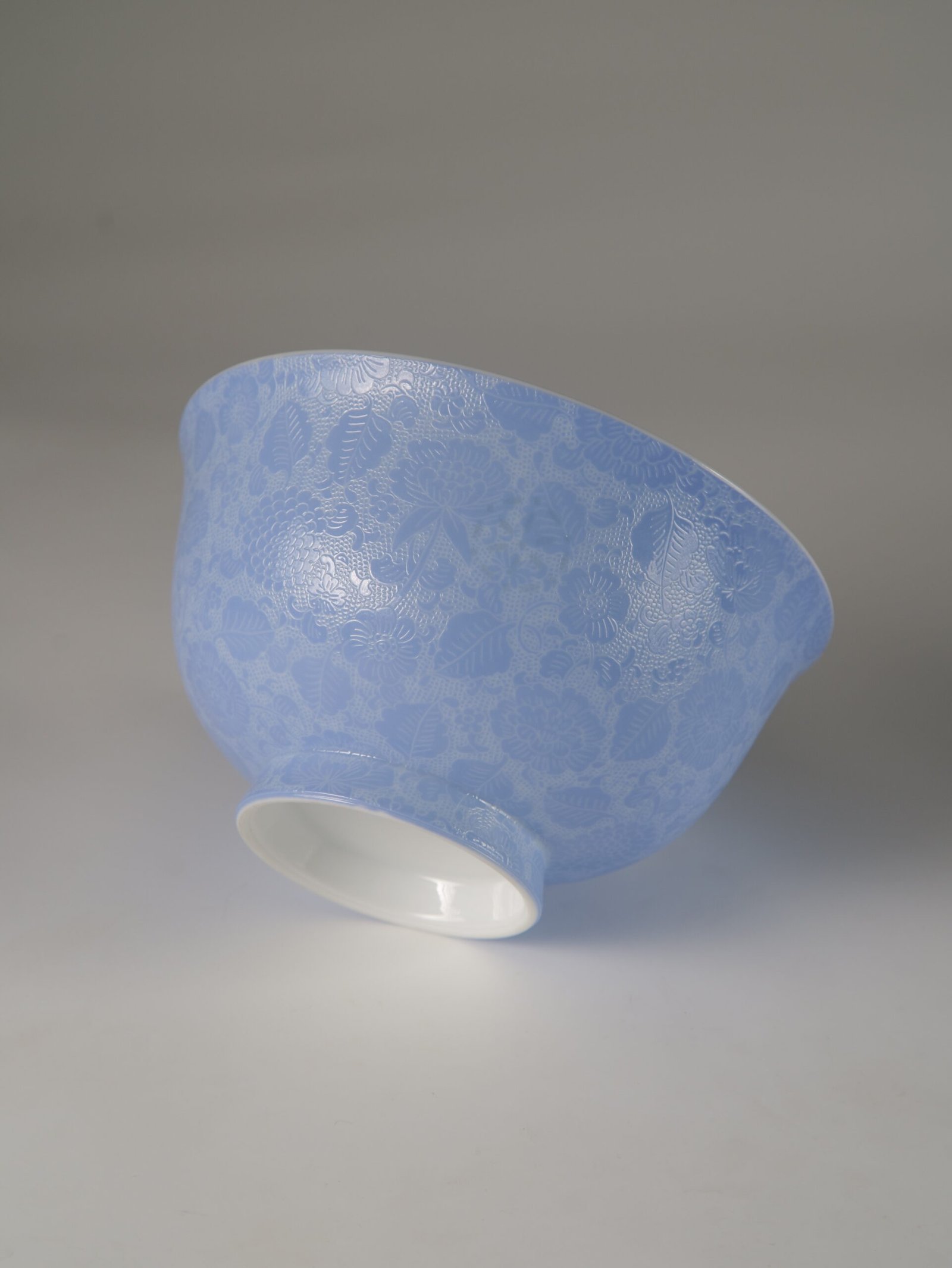 East Breaking Dawn Porcelain Bowl – Outer Carving Detail Tilted view of light blue porcelain bowl displaying carved flower texture and foot rim