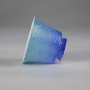 Side profile of the East Breaking Dawn gradient blue porcelain horseshoe cup lying horizontally, showcasing its elegant curve and intricate lace-like engraved pattern
