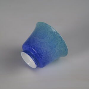 Tilted base perspective of the East Breaking Dawn gradient blue porcelain horseshoe cup highlighting its smooth foot rim and vibrant carved floral textures