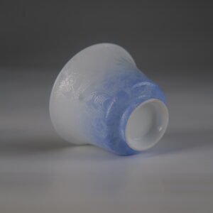Tilted view of the East Breaking Dawn gradient blue porcelain horseshoe cup highlighting the bottom foot rim and intricate carved texture