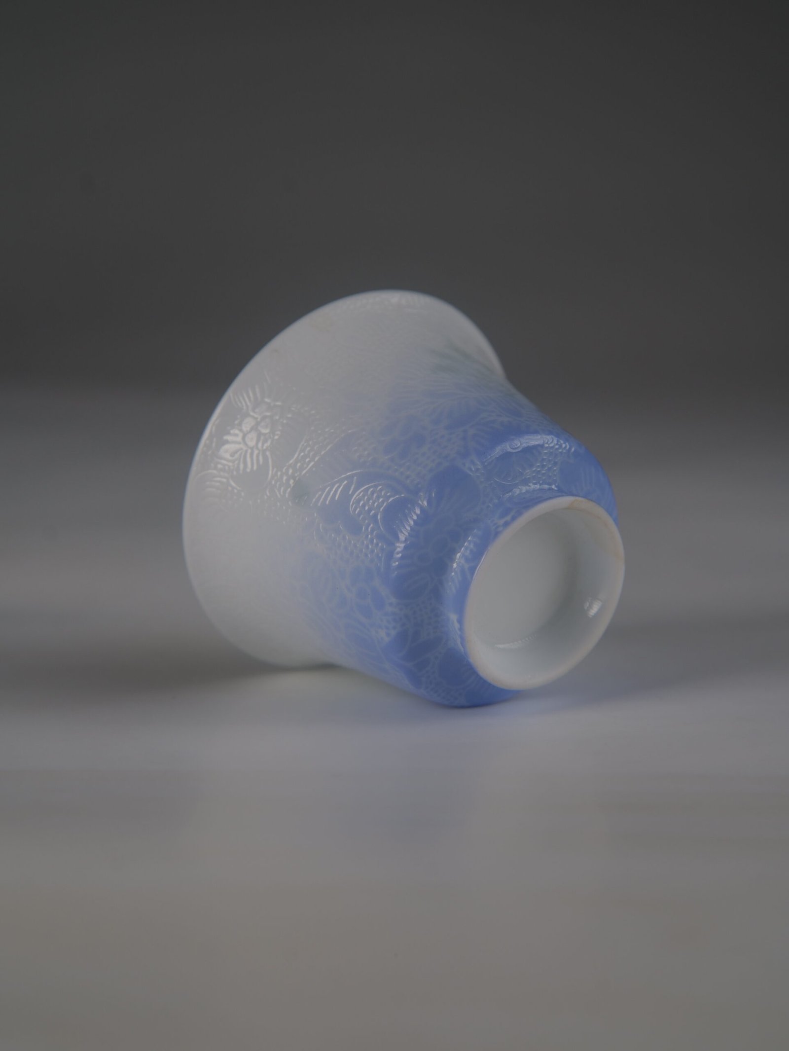 east-breaking-dawn-gradient-blue-horseshoe-porcelain-cup-bottom-detail Tilted view of the East Breaking Dawn gradient blue porcelain horseshoe cup highlighting the bottom foot rim and intricate carved texture