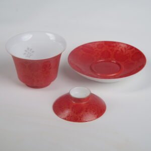 Top-angle view of the disassembled Gold-base Vermilion Horseshoe Gaiwan set with its cup, lid, and saucer placed separately, showing the rich royal red glaze on real gold powder base, the white porcelain interior with openwork daylily patterns, and intricate Pa Hua engravings
