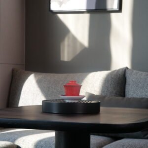 Lifestyle view of the Gold-base Vermilion Horseshoe Gaiwan set on a wooden tea tray under warm natural sunlight in a modern interior setting
