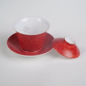 Side view of the Gold-base Vermilion Horseshoe Gaiwan with its lid removed and resting beside the saucer, showing the white porcelain interior with subtle light-transmitting effect, rich royal vermilion glaze on gold base, and fine engraved Pa Hua daylily patterns