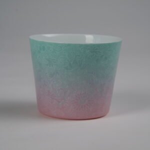 Eye level back view of green and pink gradient porcelain cup with interlocking lotus motif