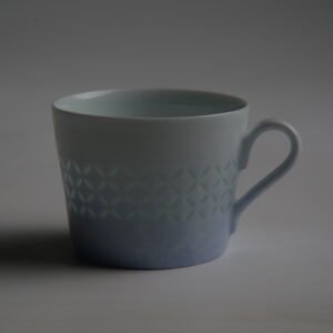 Darkened side view of light blue gradient porcelain coffee cup with handle
