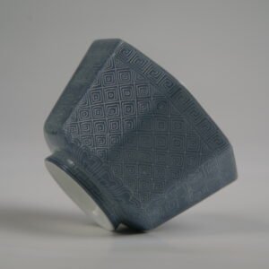 Tilted side view of the Lunar Gray Octagonal porcelain cup lying on its side, showcasing its geometric shape, solid lunar gray glaze, and intricate engraved Pa Hua lattice and Taotie patterns