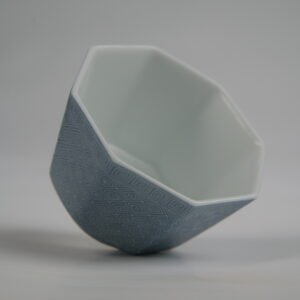 Top-angle interior view of the Lunar Gray Octagonal porcelain cup lying tilted, showing its octagonal rim, white interior, and solid lunar gray outer body with fine engraved Pa Hua lattice textures