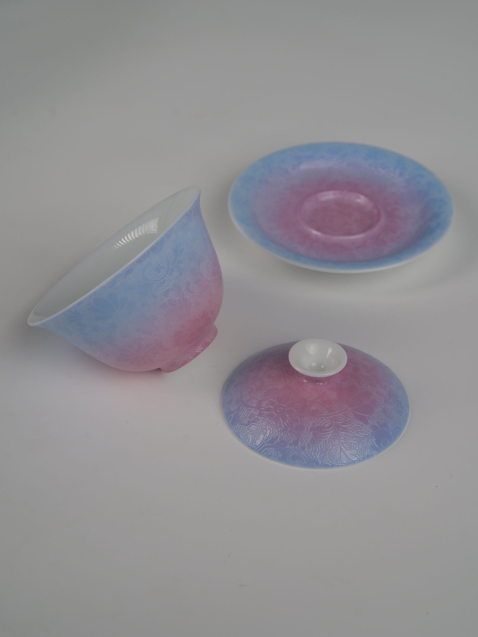 midsummer-dream-gradient-elegant-charm-gaiwan-disassembled-three-piece-view Disassembled view of the Midsummer Dream Gradient Elegant Charm Gaiwan showing the lid, cup, and saucer set separately, highlighting the soft pale purple and pink gradient glaze and handcrafted Pa Hua Hundred Flowers pattern