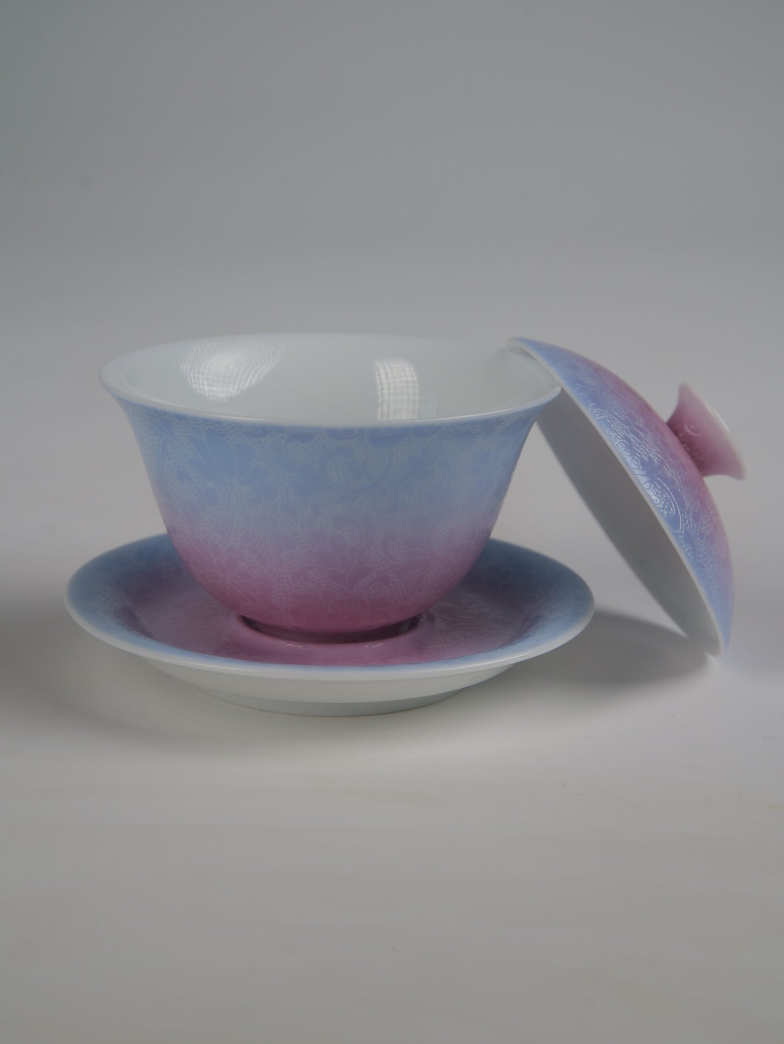 midsummer-dream-gradient-elegant-charm-gaiwan-open-lid-view Side view of the Midsummer Dream Gradient Elegant Charm Gaiwan with its lid removed and resting beside the saucer, showing the white porcelain interior, the soft gradient blend of pale purple and pink glaze, and the handcrafted Pa Hua floral pattern
