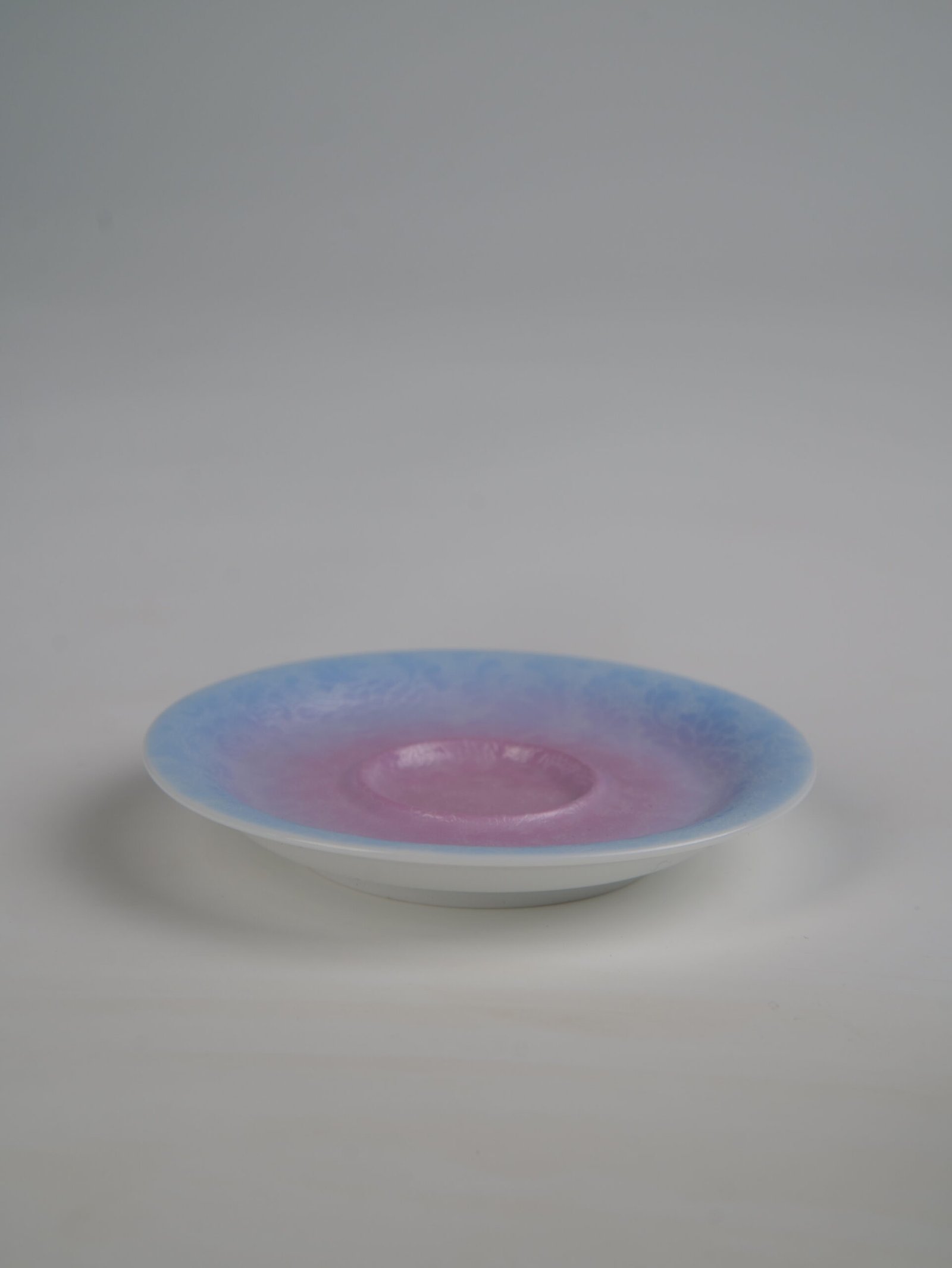 midsummer-dream-gradient-elegant-charm-gaiwan-saucer-only-view Side angle view of the standalone saucer from the Midsummer Dream Gradient Elegant Charm Gaiwan, showcasing the soft pale purple and pink gradient glaze and intricate hand-carved Pa Hua floral pattern