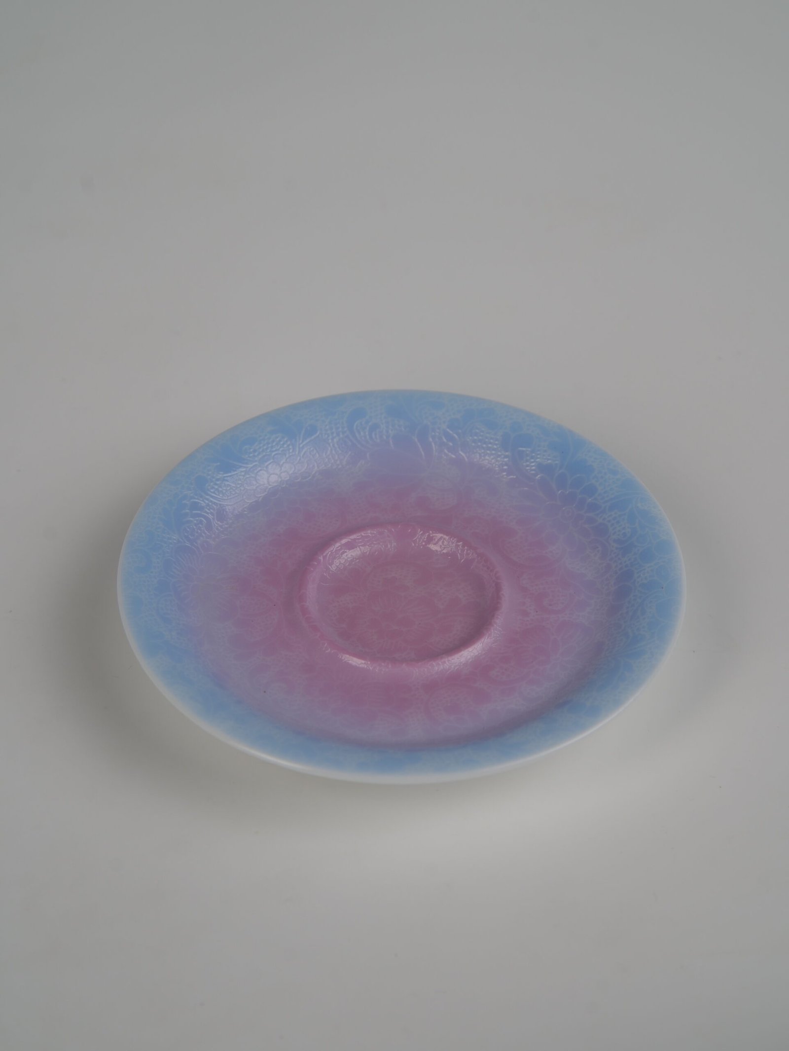 midsummer-dream-gradient-elegant-charm-gaiwan-saucer-top-angle-view Top-angle view of the standalone saucer from the Midsummer Dream Gradient Elegant Charm Gaiwan, showcasing the soft pale purple and pink gradient glaze and intricate hand-carved Pa Hua Hundred Flowers pattern