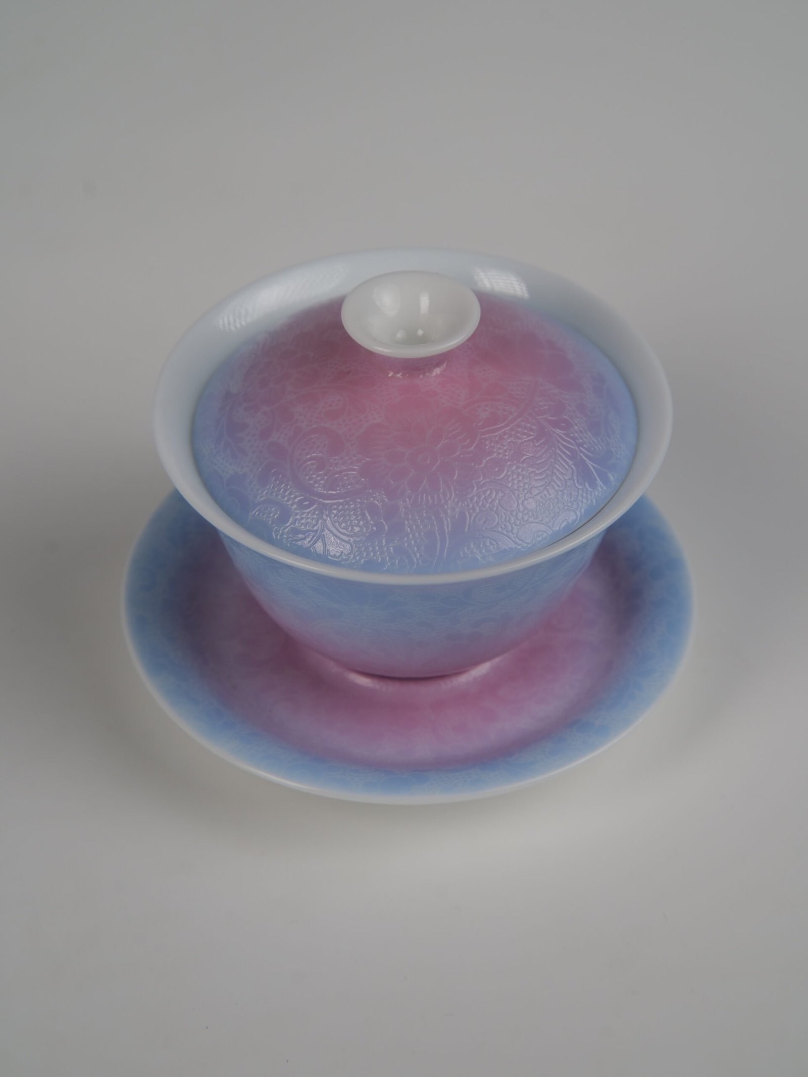 midsummer-dream-gradient-elegant-charm-gaiwan-top-angle-view Top-angle view of the Midsummer Dream Gradient Elegant Charm Gaiwan full set, showcasing the soft gradient blend of pale purple and pink glaze on lid and saucer with fine hand-carved Pa Hua Hundred Flowers floral pattern