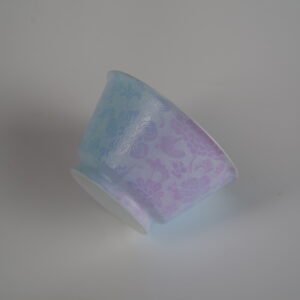 Side profile view of the Misty Lavender Haze Linked-loop porcelain cup lying on its side, showing its soft pastel gradient and delicate carved floral texture