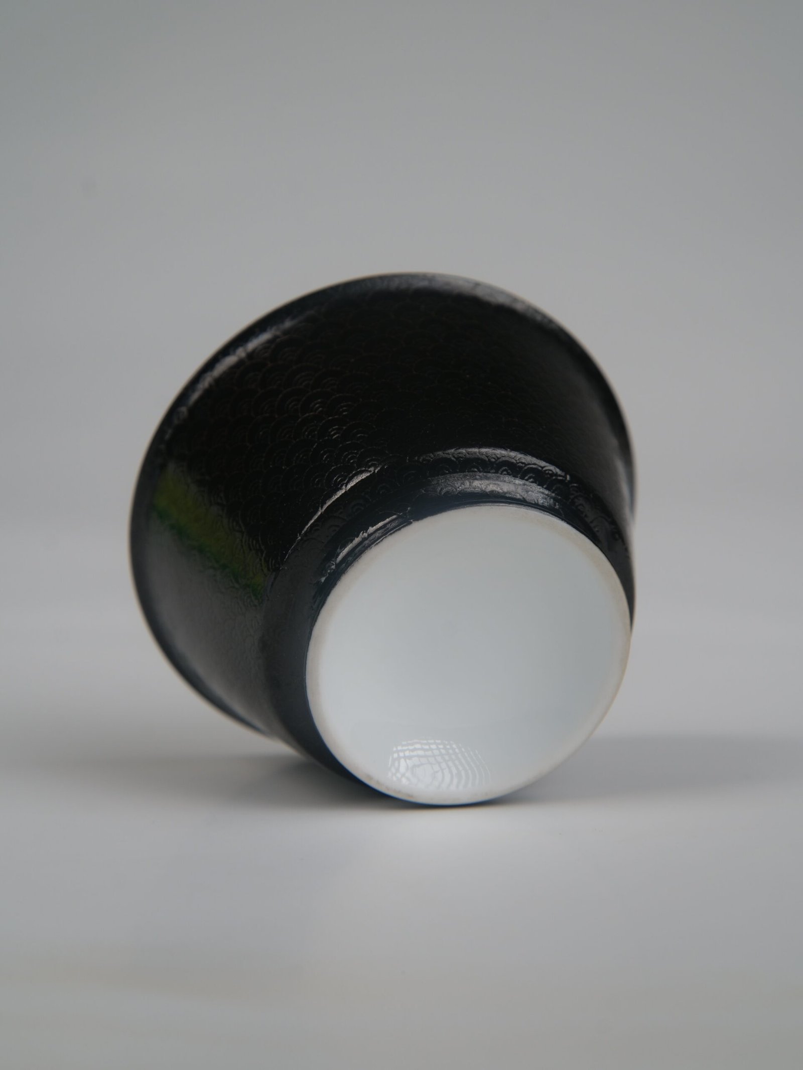 obsidian-black-linked-loop-porcelain-cup-bottom-base-center-view Centered bottom view of the Obsidian Black Linked-loop porcelain cup, showcasing its smooth white circular base and dark carved dragon scale body