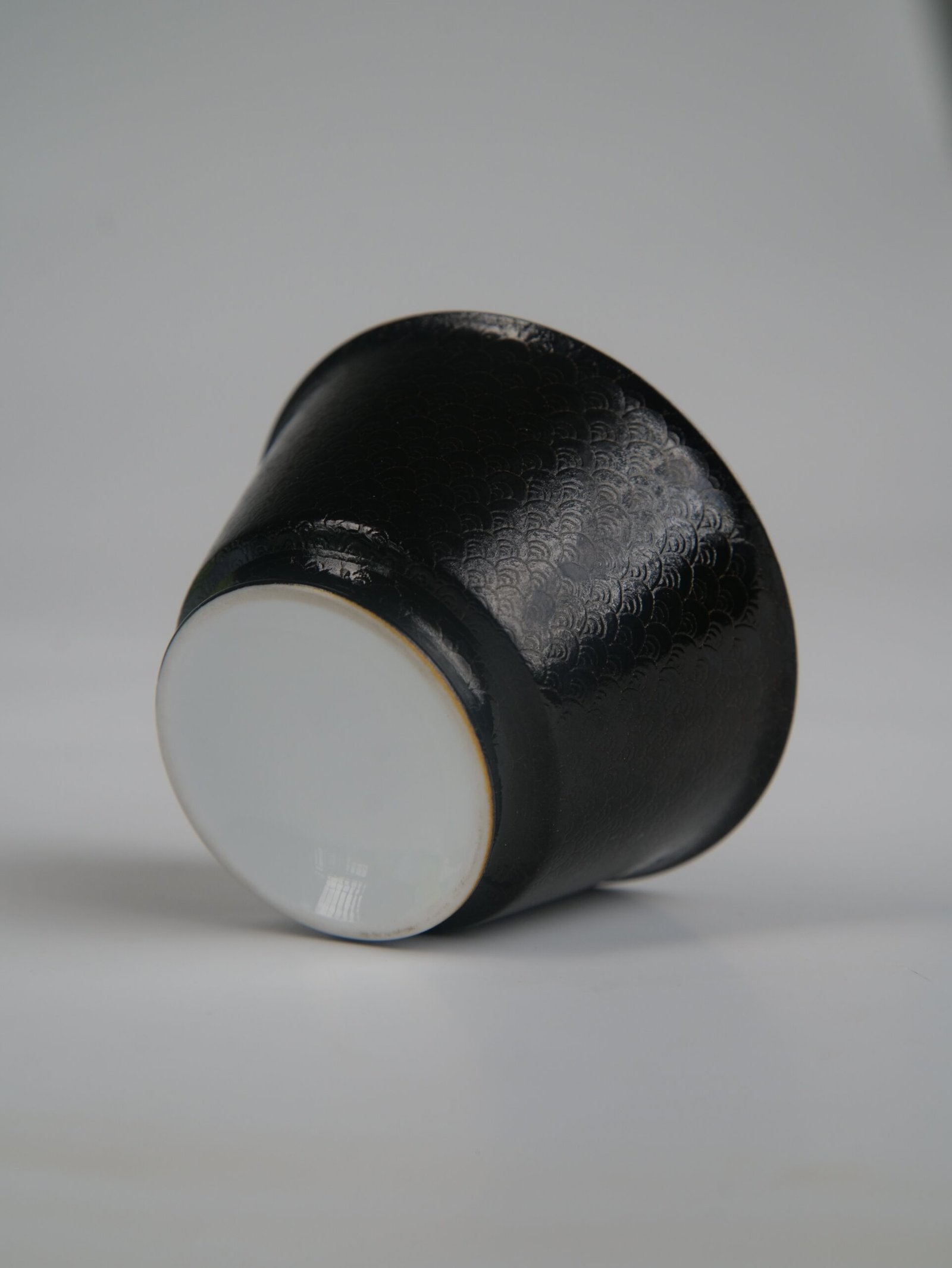 obsidian-black-linked-loop-porcelain-cup-bottom-up-view Bottom-up view of the Obsidian Black Linked-loop porcelain cup showcasing its white circular base and detailed dark carved enamel dragon scale pattern