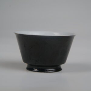 Front view of the Obsidian Black Linked-loop porcelain cup showing its dark carved enamel dragon scale body and white interior