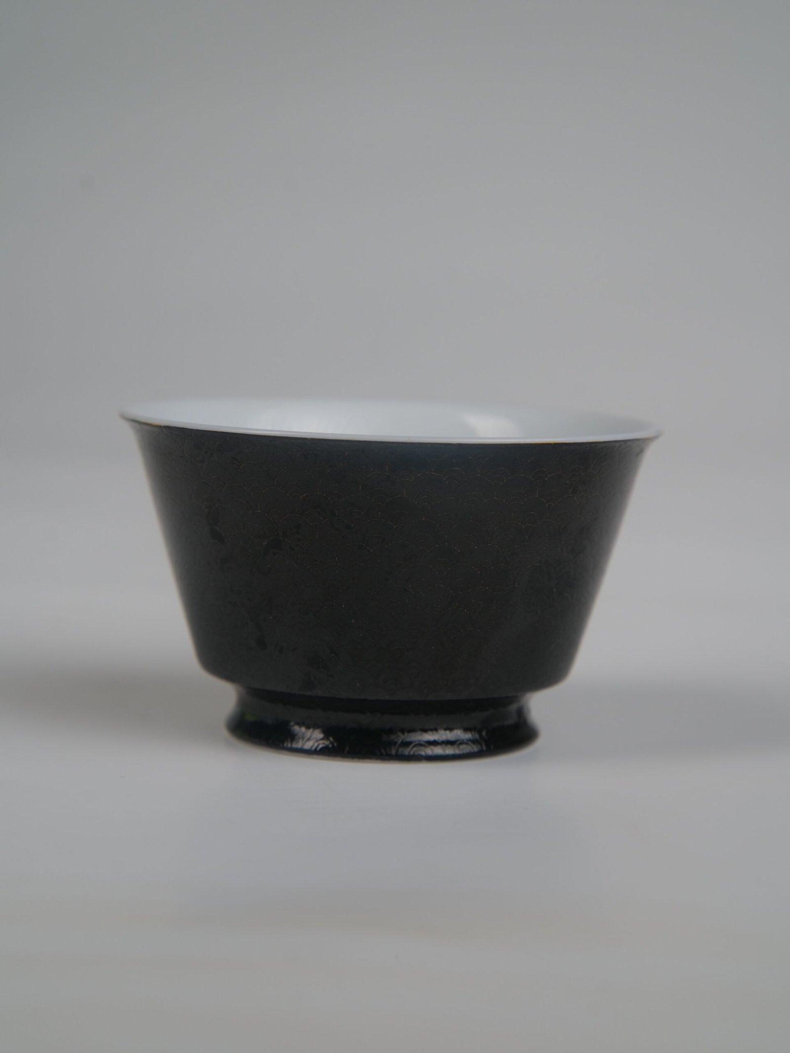 obsidian-black-linked-loop-porcelain-cup-front-view Front view of the Obsidian Black Linked-loop porcelain cup showing its dark carved enamel dragon scale body and white interior