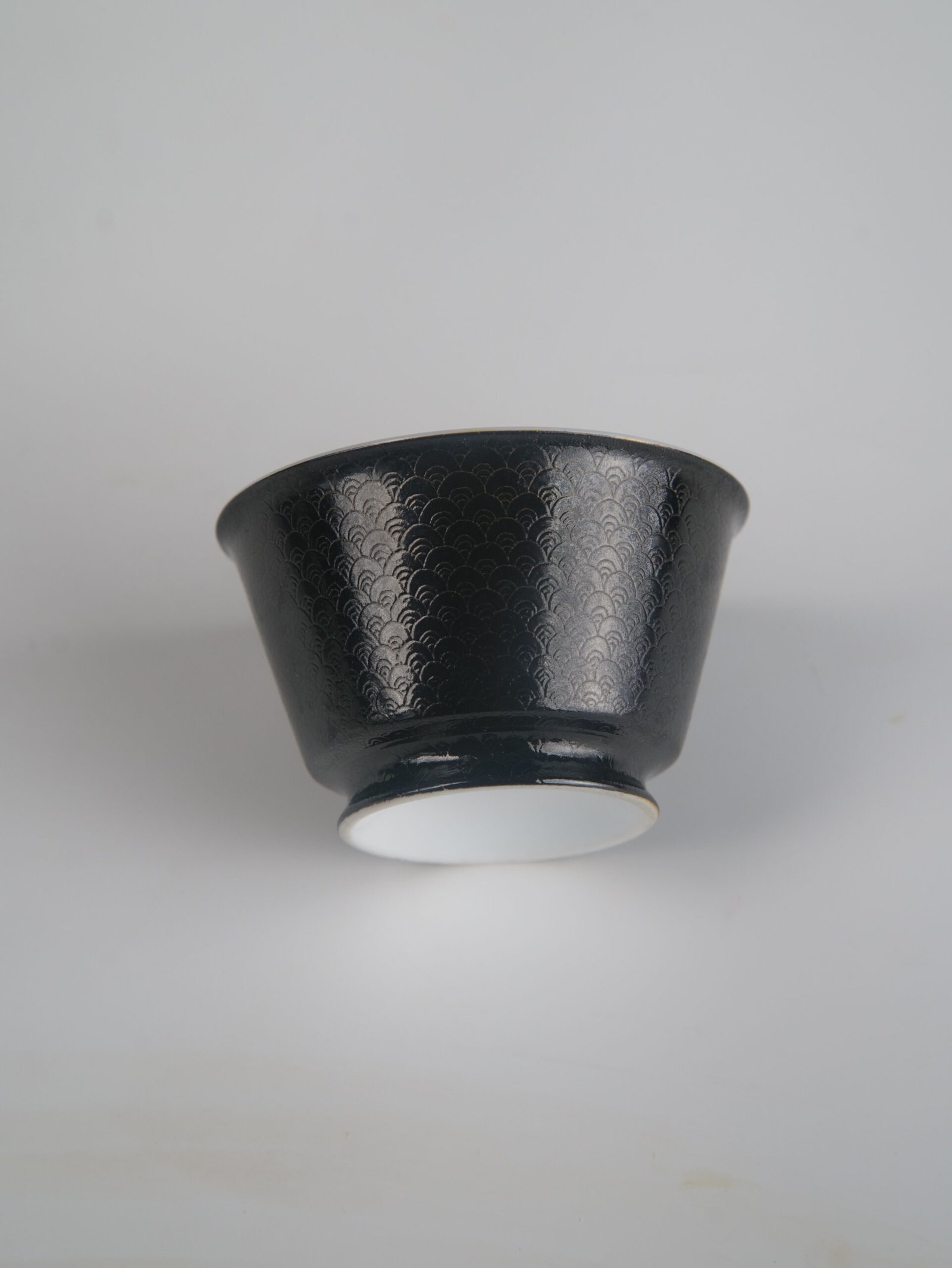 obsidian-black-linked-loop-porcelain-cup-low-angle-view Low-angle view of the Obsidian Black Linked-loop porcelain cup highlighting its white foot base and detailed dark carved enamel dragon scale texture