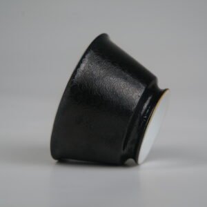 Side profile view of the Obsidian Black Linked-loop porcelain cup lying on its side, highlighting its dark carved enamel dragon scale pattern and smooth base