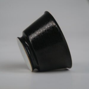 Tilted side view of the Obsidian Black Linked-loop porcelain cup lying on its side, showing its elegant curve, foot base, and carved dragon scale texture