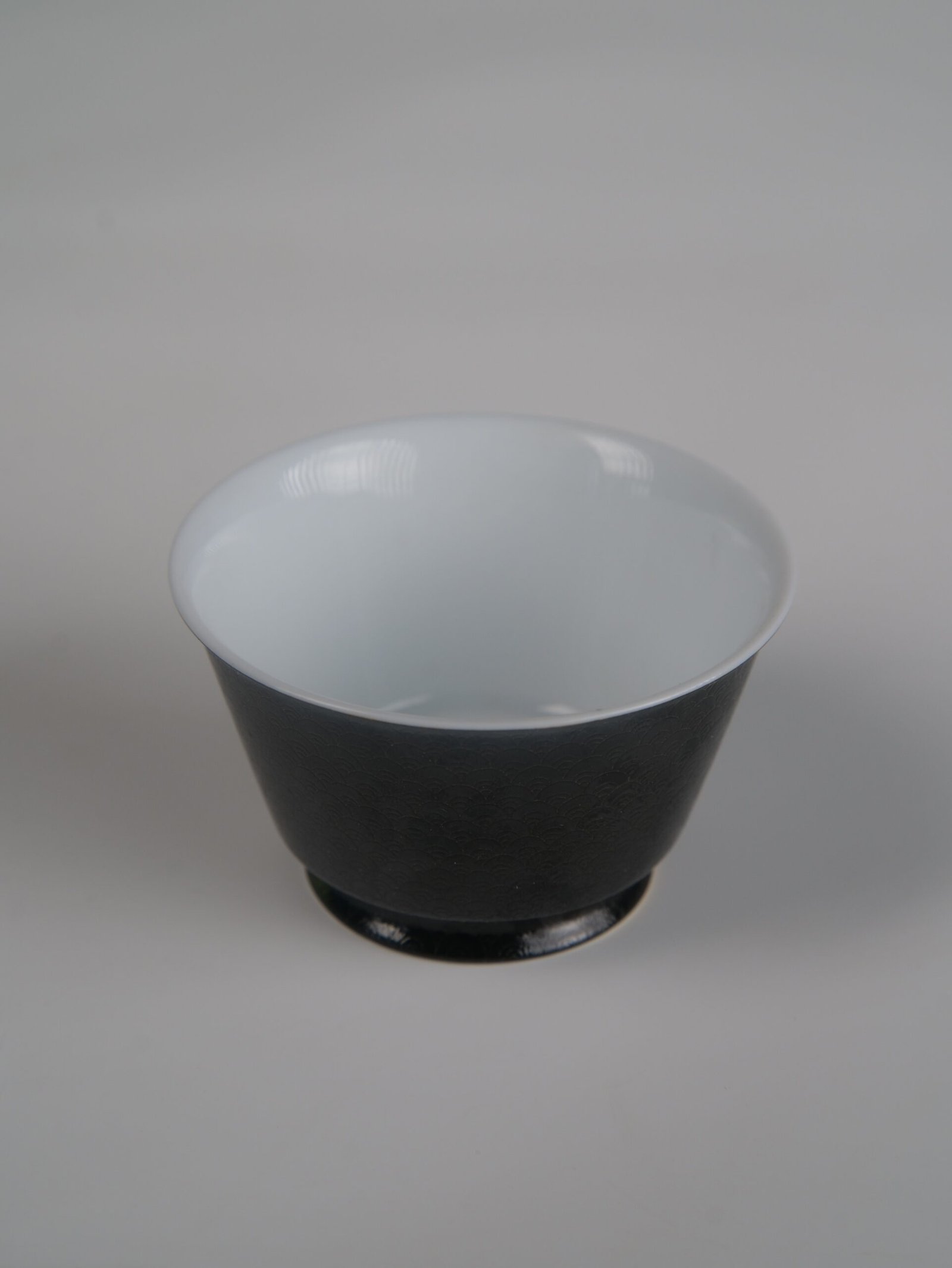 obsidian-black-linked-loop-porcelain-cup-top-down-view Top-down view of the Obsidian Black Linked-loop porcelain cup featuring a smooth white interior and dark carved dragon scale exterior
