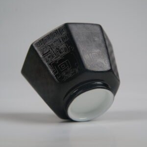 Bottom-angle view of the Obsidian Black Octagonal porcelain cup showcasing its white base, geometric octagonal structure, deep obsidian black glaze, and fine engraved Shang Dynasty Taotie and lattice patterns