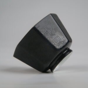 Tilted side view of the Obsidian Black Octagonal porcelain cup lying on its side, showcasing its geometric shape, deep obsidian black glaze, and intricate engraved Pa Hua lattice and Taotie patterns