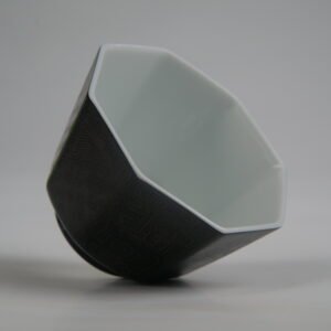 Top-angle interior view of the Obsidian Black Octagonal porcelain cup lying tilted, showing its octagonal rim, white interior, and solid obsidian black outer body with fine engraved Pa Hua lattice textures