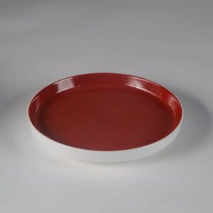 Angled view of round palace red porcelain plate with white exterior edge