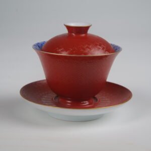 A detailed studio view of the Palace Red Elegant Charm Gaiwan set with lid and saucer on a plain white background, highlighting the intricately textured red body and gold rim.