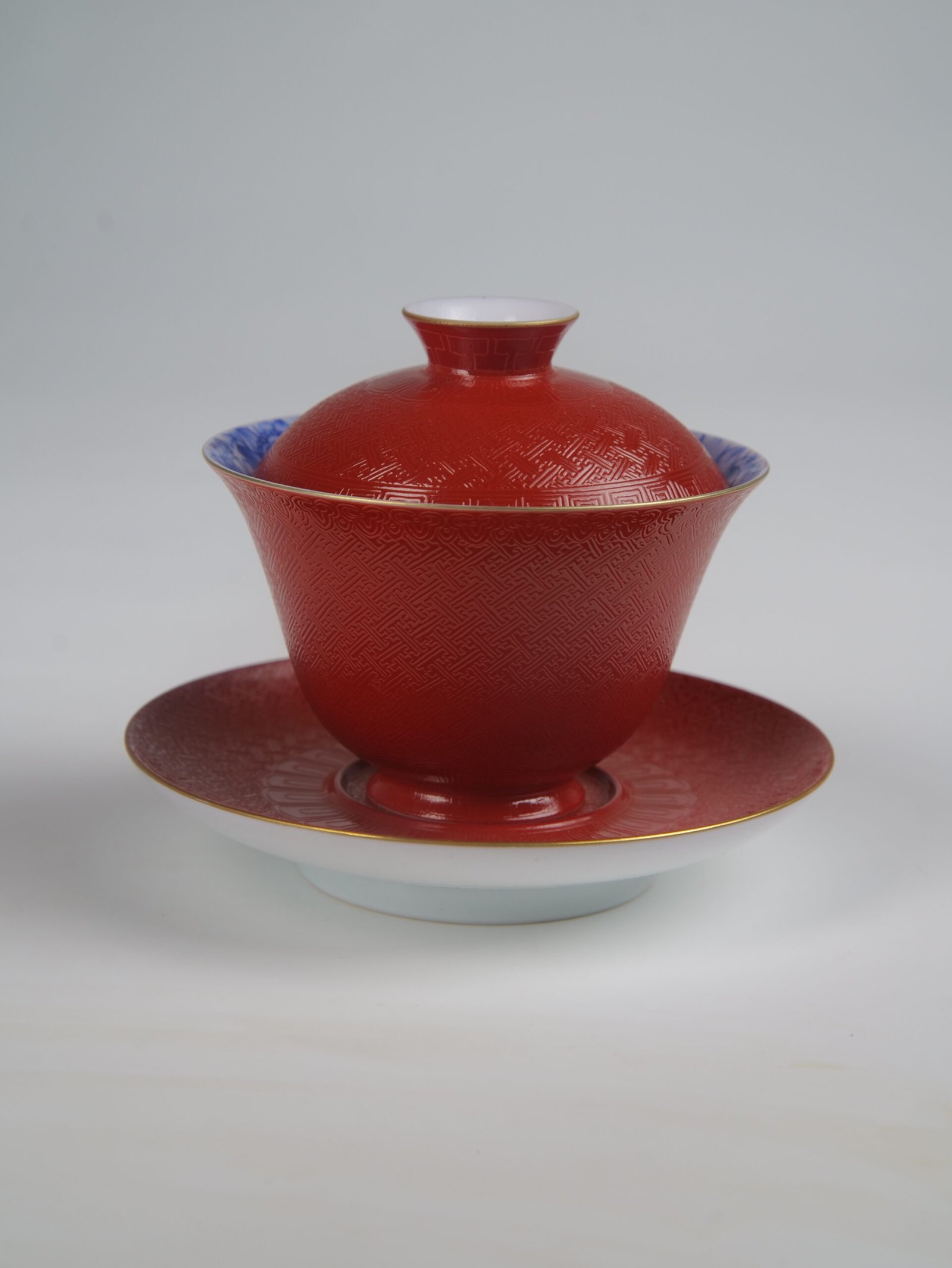 palace-red-elegant-charm-gaiwan-studio-view A detailed studio view of the Palace Red Elegant Charm Gaiwan set with lid and saucer on a plain white background, highlighting the intricately textured red body and gold rim.