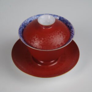 An overhead perspective view of the Palace Red Elegant Charm Gaiwan set, showcasing the intricate woven texture on the red lid and saucer, and the blue and white patterned interior rim.