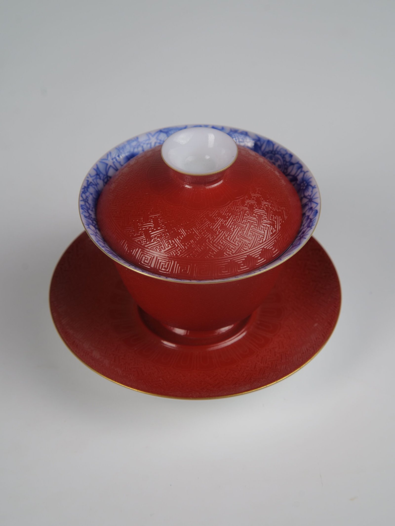 palace-red-elegant-charm-gaiwan-top-angle-textured An overhead perspective view of the Palace Red Elegant Charm Gaiwan set, showcasing the intricate woven texture on the red lid and saucer, and the blue and white patterned interior rim.