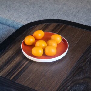 Palace red porcelain plate holding fresh kumquats on wooden table