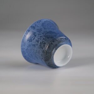 Angled view of the base of the Pale Ink Pool blue porcelain horseshoe cup, showing the smooth white bottom rim and full floral carving detail