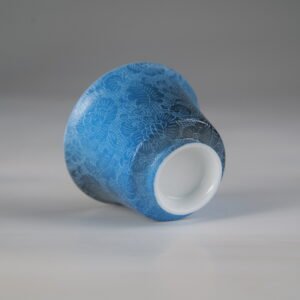 An angled bottom-up view of the Pale Ink Pool blue porcelain horseshoe cup highlighting its smooth white base rim and detailed body carving