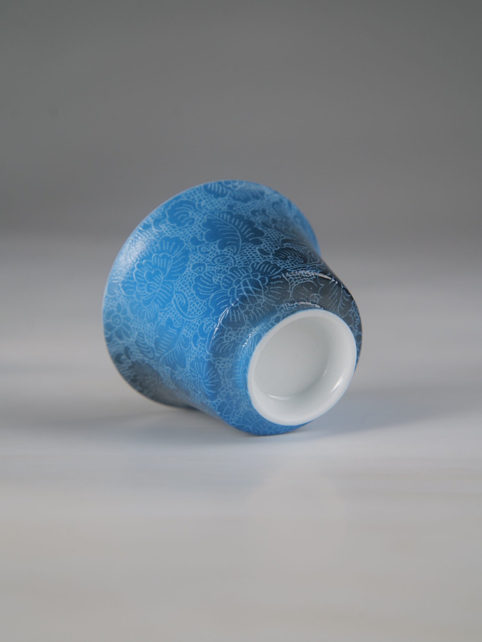pale-ink-pool-blue-horseshoe-porcelain-cup-bottom-rim-detail An angled bottom-up view of the Pale Ink Pool blue porcelain horseshoe cup highlighting its smooth white base rim and detailed body carving