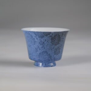 Front view of the Pale Ink Pool blue porcelain horseshoe cup featuring deep blue glaze and intricate full-body floral engraving